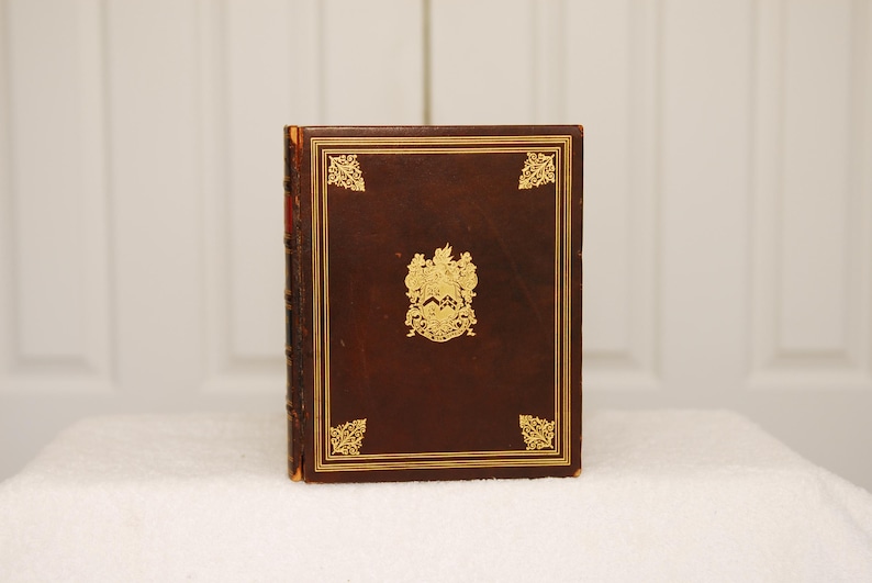 May include: A brown leather-bound book with gold accents and a gold crest on the front cover.
