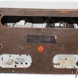May include: Rear view of a vintage wooden radio cabinet. The brown cabinet has a rectangular opening showing internal components. A UL sticker is visible. Model number 4218 is printed on a metal plate.