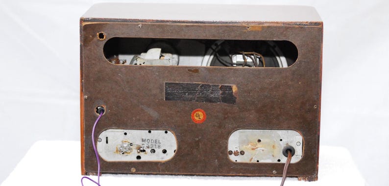 May include: Rear view of a vintage wooden radio cabinet. The brown cabinet has a rectangular opening showing internal components. A UL sticker is visible. Model number 4218 is printed on a metal plate.