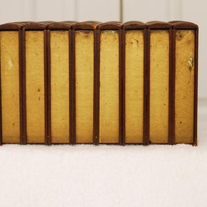 May include: A set of eight brown leather-bound books with gold accents. The books are arranged in a row on a white surface.