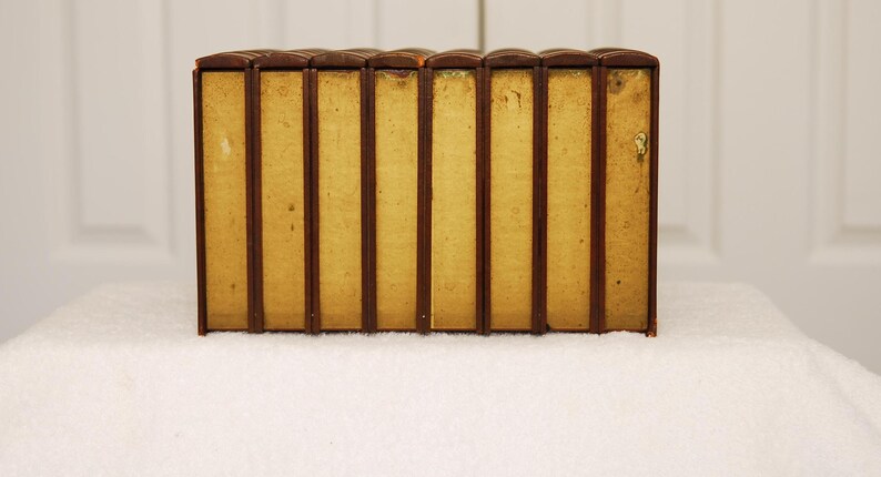 May include: A set of eight brown leather-bound books with gold accents. The books are arranged in a row on a white surface.