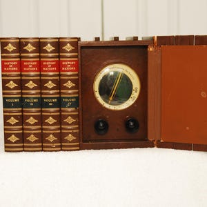 May include: A vintage wooden radio with a round dial and two knobs. The radio is sitting on a white surface and is surrounded by four books titled "History of Nations" with volume numbers I, II, III, and IV.