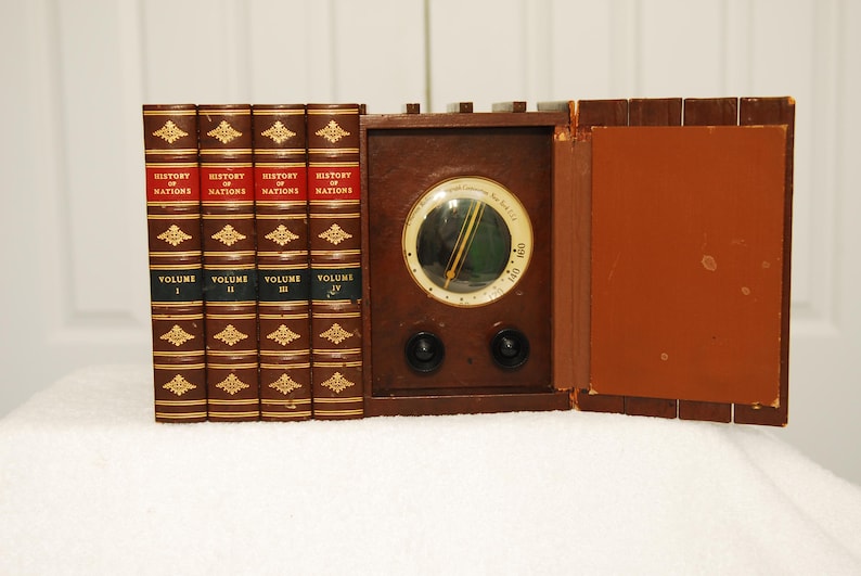 May include: A vintage wooden radio with a round dial and two knobs. The radio is sitting on a white surface and is surrounded by four books titled "History of Nations" with volume numbers I, II, III, and IV.