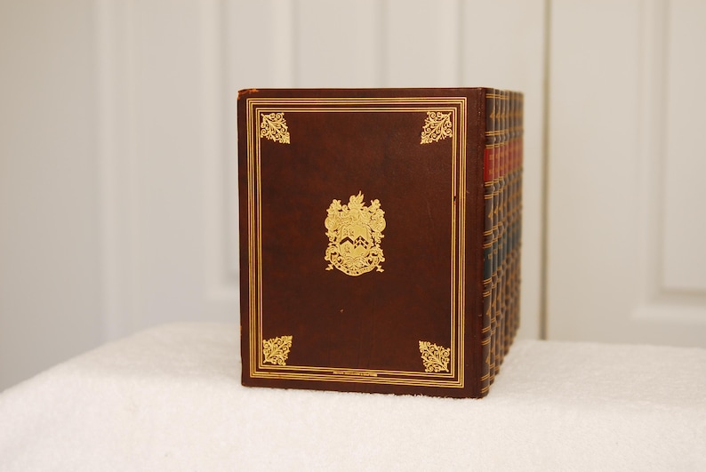 May include: A set of brown leather-bound books with gold accents and a crest on the front cover.