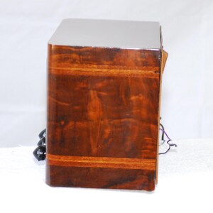May include: A vintage wooden radio with a glossy, dark brown finish. The radio has a rectangular shape with rounded edges and a contrasting lighter wood band. Black knobs and wires are visible on the side.