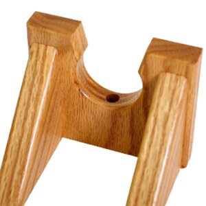 May include: A wooden wall mount stand for displaying a guitar. The stand is made of light brown wood and has a rounded opening in the center to hold the guitar's neck.