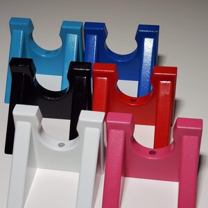 May include: A collection of colorful, H-shaped wooden stands. The stands are painted in various colors, including light blue, black, white, red, pink, and dark blue. Each stand has a curved top and two vertical legs.