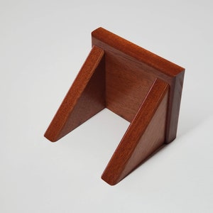 May include: A wooden wall mount shelf with a reddish-brown finish. The shelf is angled and has a triangular shape.