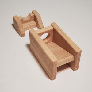 May include: A wooden stand with two levels, the top level has a round hole in the front. The stand is made of light brown wood.