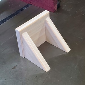May include: A simple wooden shelf unit with two angled supports. The shelf is made of unfinished pine wood.