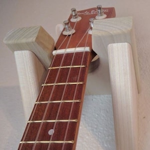 May include: A wooden wall mount guitar hanger with a ukulele hanging on it. The hanger is made of natural wood and has a simple design.