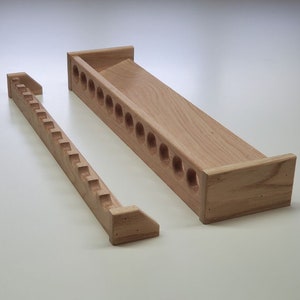 May include: Two wooden racks, one long with a series of circular holes and the other with a series of notches. Both are made of light-colored wood. The longer rack has a rectangular shape with a series of circular holes. The shorter rack has a series of notches.