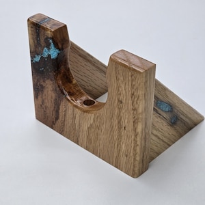 May include: A wooden stand with a natural finish and turquoise accents. The stand is angled, with a curved section and a small hole. The wood grain is visible, and the turquoise adds a pop of color. The stand is likely for a small item.