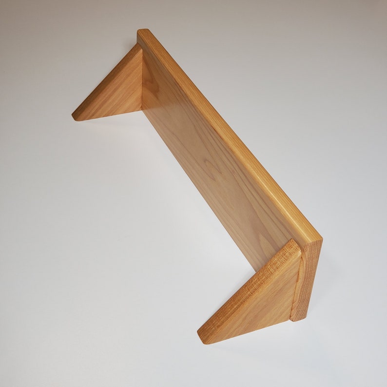 May include: A wooden shelf with triangular supports. The shelf is made of light brown wood and has a natural finish.