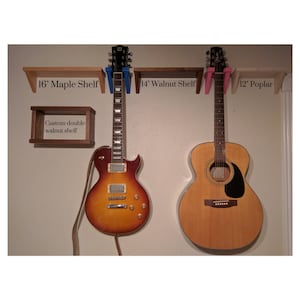 May include: Two guitars mounted on a wall with three wooden shelves. The shelves are labeled "16" Maple Shelf", "14" Walnut Shelf", and "12" Poplar". A smaller walnut shelf is labeled "Custom double walnut shelf".