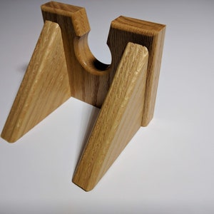 May include: A wooden stand with a triangular shape and a cutout in the center. The stand is made of light brown wood with a natural grain pattern.