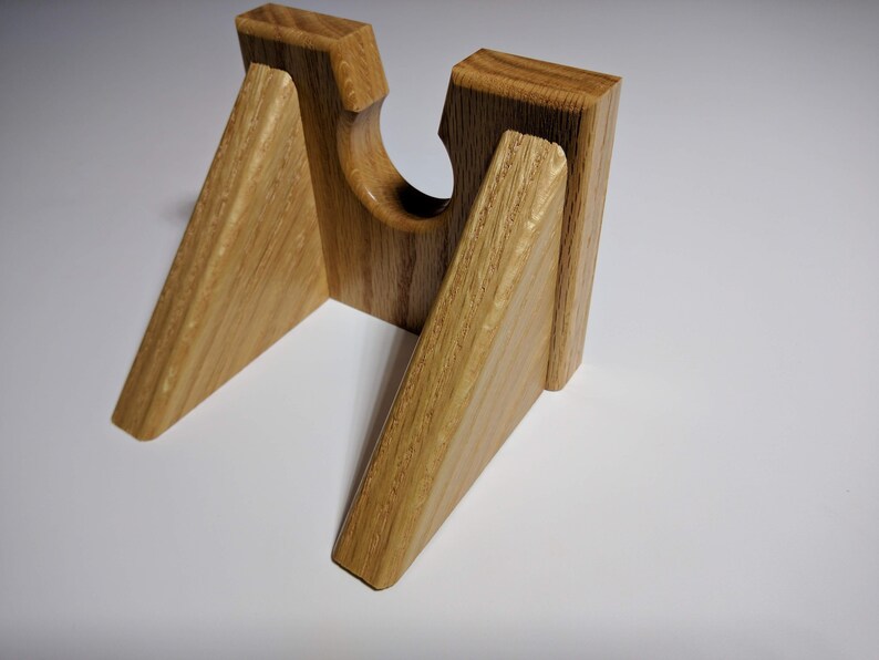 May include: A wooden stand with a triangular shape and a cutout in the center. The stand is made of light brown wood with a natural grain pattern.