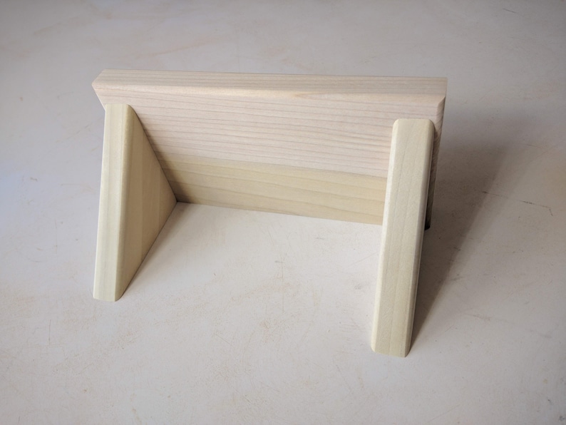 May include: A wooden stand with two triangular supports, made of light wood.