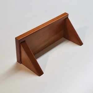 May include: A wooden shelf with a triangular support on each side. The shelf is made of natural wood with a light brown finish.
