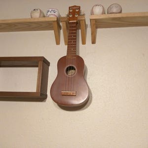 May include: A wooden shelf unit with three shelves, a small shelf on the left, a larger shelf on the right, and a smaller shelf in the middle. A ukulele is hanging from the middle shelf. There are three baseballs on the top shelf.