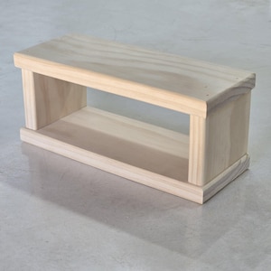 May include: A rectangular, unfinished wooden box with an open front and back. The box is made of light-colored wood and has a simple, clean design. The top and bottom are solid, while the sides are open, creating a shelf or display space.