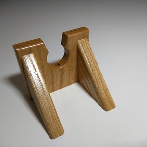 May include: A wooden stand with a cutout for a gun. The stand is made of light brown wood and has a natural finish.