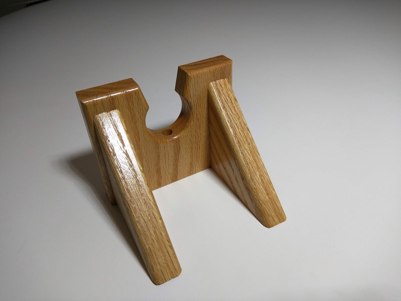 May include: A wooden stand with a cutout for a gun. The stand is made of light brown wood and has a natural finish.