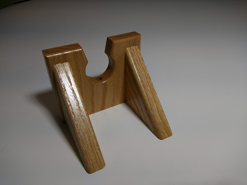 May include: A wooden stand with a cutout for a bottle or other object. The stand is made of light brown wood and has a simple design.
