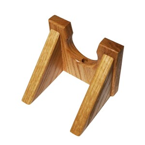 May include: A wooden wall mount stand for a guitar or other musical instrument. The stand is made of light brown wood and has a simple, sturdy design.