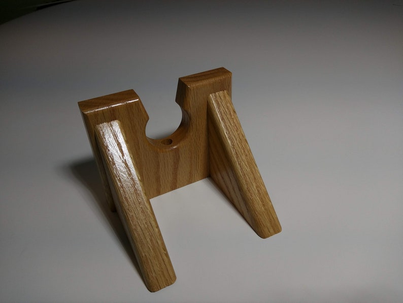 May include: A wooden stand with a cutout for holding a small object, such as a phone or a tablet. The stand is made of light brown wood and has a simple, modern design.