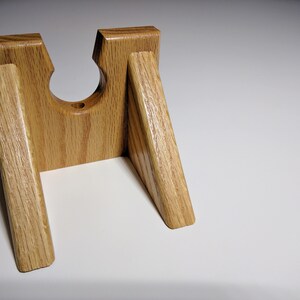 May include: A wooden stand with a circular cutout in the center, designed to hold a bottle or other cylindrical object. The stand is made of light brown wood with a natural grain pattern.