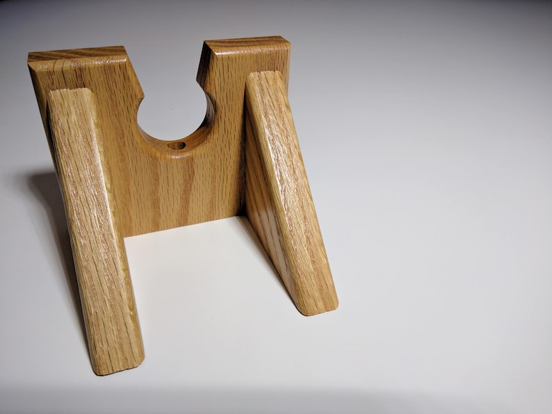 May include: A wooden stand with a circular cutout in the center, designed to hold a bottle or other cylindrical object. The stand is made of light brown wood with a natural grain pattern.
