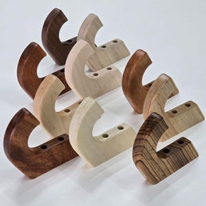 May include: Eight wooden hooks in various wood tones, including light brown, dark brown, and reddish brown. The hooks are all shaped like a curved 'C' and have three holes drilled into the back for mounting.