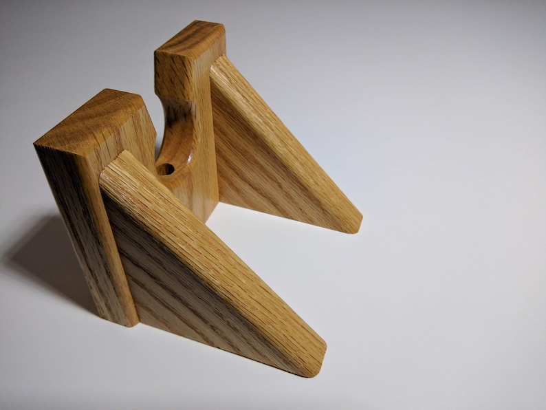 May include: A wooden wall mount with two angled shelves, designed to hold a guitar. The mount is made of light brown wood with a natural grain pattern.