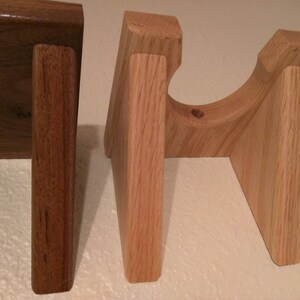 May include: Three wooden guitar stands, two are light brown and one is dark brown. The stands are made of solid wood and have a simple design.