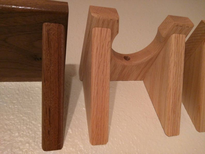 May include: Three wooden guitar stands, two are light brown and one is dark brown. The stands are made of solid wood and have a simple design.
