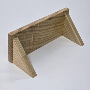 May include: A wooden shelf with a natural finish. The shelf has a rectangular top supported by two triangular legs. The wood grain is visible, and the shelf is designed to sit on a flat surface.