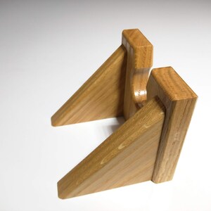 May include: A wooden wall mount with two angled shelves, designed to hold a pair of headphones.