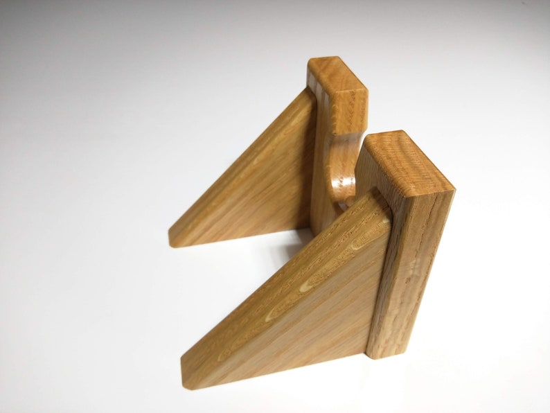 May include: A wooden wall mount with two angled shelves, designed to hold a pair of headphones.