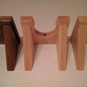 May include: Three wooden wall mounts, two are light brown and one is dark brown. The light brown mounts are shaped like a U and have a round hole in the center. The dark brown mount is a simple rectangular shape.