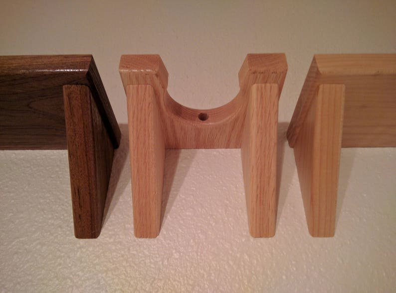 May include: Three wooden wall mounts, two are light brown and one is dark brown. The light brown mounts are shaped like a U and have a round hole in the center. The dark brown mount is a simple rectangular shape.