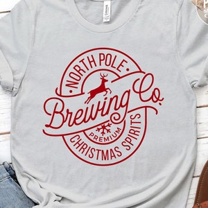 May include: A gray t-shirt with a red circle design that says "North Pole Brewing Co." with a reindeer inside the circle. The text "Premium Christmas Spirits" is written around the circle.