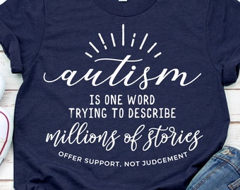May include: A navy blue t-shirt with white text that reads "autism is one word trying to describe millions of stories offer support, not judgement". The text is in a stylized font with a sunburst design above the word "autism".
