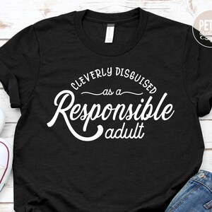 May include: A black t-shirt with white text that reads "Cleverly Disguised as a Responsible Adult".