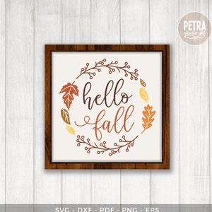 May include: A framed print with the words "hello fall" in brown script, encircled by a wreath of autumn leaves in orange, yellow, and brown. The wooden frame surrounds a white background. The words "DIGITAL DOWNLOAD" are at the bottom.