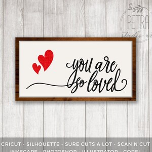 May include: A white sign with a brown frame, featuring the text "you are so loved" in black cursive script. Three red hearts are placed above the text.