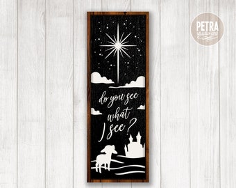 May include: Black and white silhouette design of a lamb looking up at a star with the text "do you see what I see?" and a castle in the background. The design is on a black background with a wood frame.