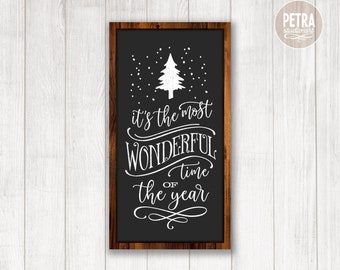 May include: A framed black sign with white text that reads "It's the most wonderful time of the year." A white Christmas tree and snowflakes are above the text. The frame is brown and the background is a white wood.