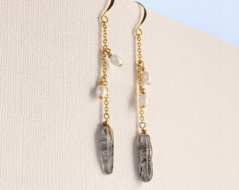 May include: A pair of long gold dangle earrings with a gray crystal and white pearl accents.