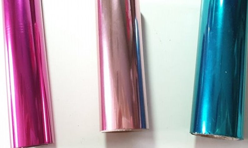 May include: Three rolls of metallic wrapping paper. The rolls are pink, rose gold, and teal.